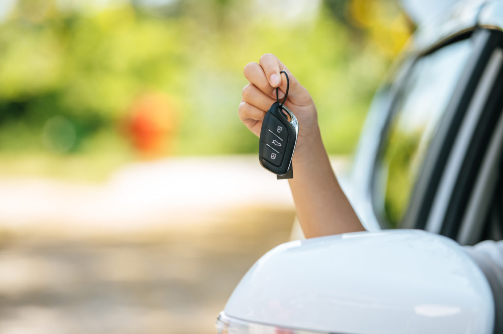 Na imagem há uma pessoa segurando a chave de um carro, apoiando o braço na janela de um carro