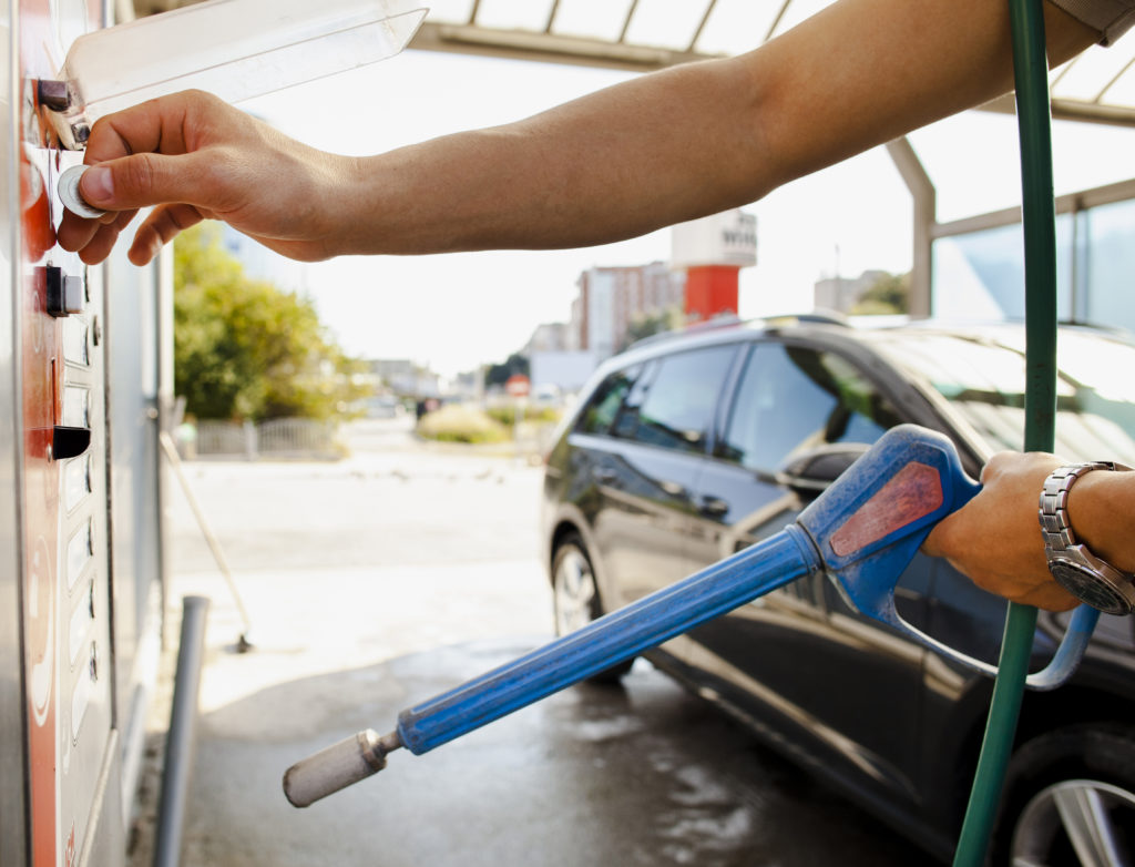 pessoa abastecendo carro preto em um posto de gasolina, com uma mangueira de combustível azul