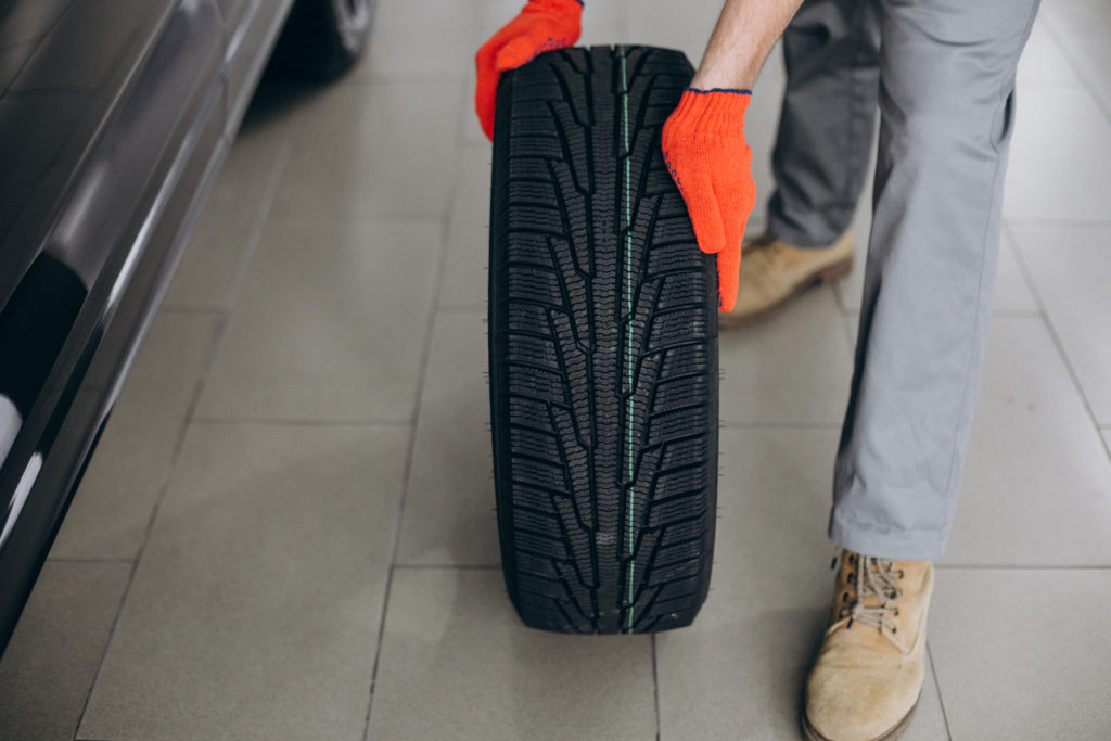 Na imagem há uma pessoa com as duas mão apoiadas em um pneu, avaliando aspectos do pneu.