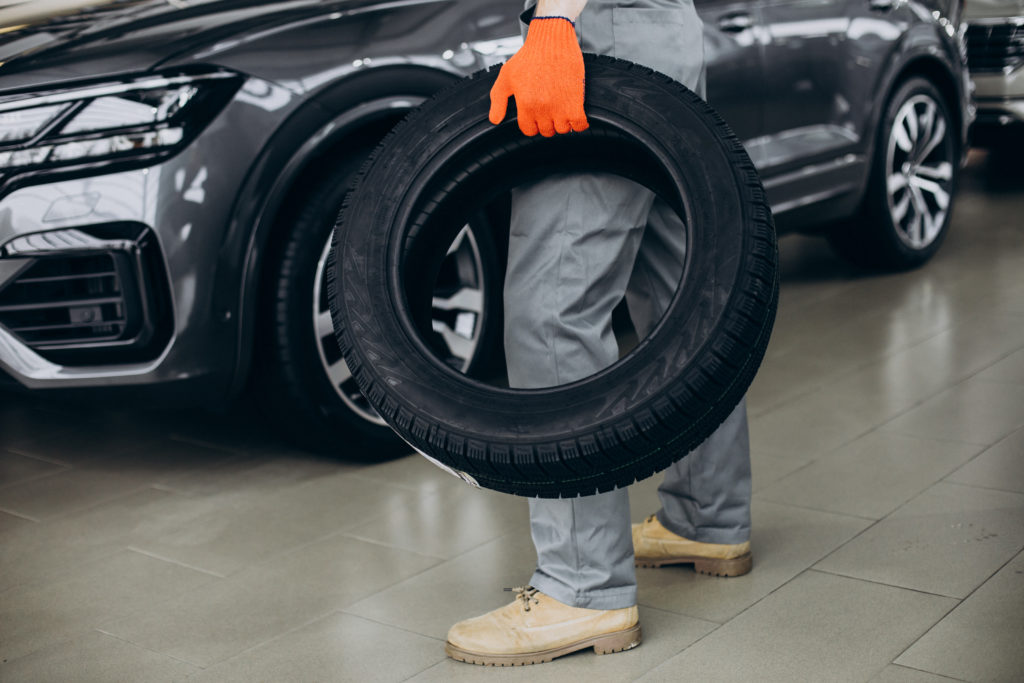 Na imagem há uma pessoa segurando com a mão esquerda um pneu com uma luva laranja.