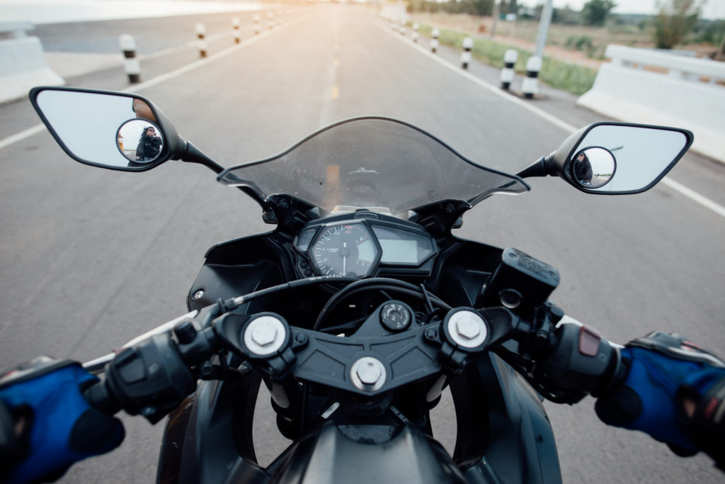 Imagem da visão do motociclista dirigindo uma moto da cor preta.