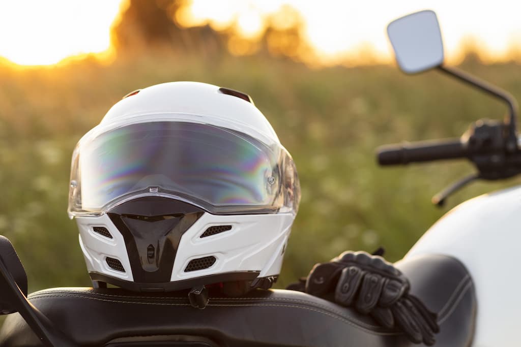 Na imagem há uma moto, com capacete e luvas apoiadas no banco.