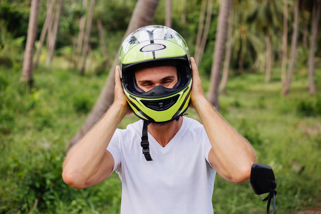 Na imagem há uma pessoa com dificuldade em colocar um dos tipos de capacete de moto, por causa do tamanho.