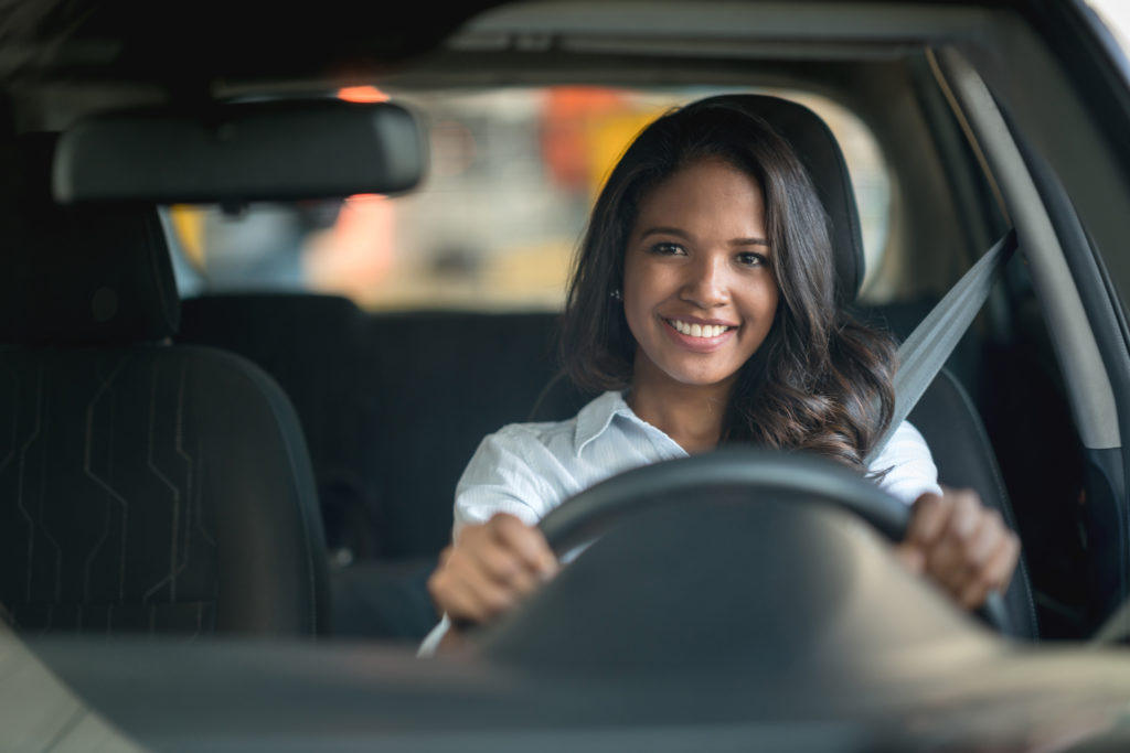 Na imagem há uma motorista parceira 99, segurando o volante com as duas mãos e sorrindo.