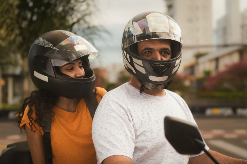 Na imagem há um motociclista parceiro 99 e uma passageira trafegando em uma moto. Ambos estão usando capacete. 